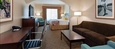 A hotel room with a bed, a desk, a chair, a sofa, and a TV.