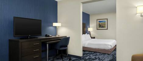 A hotel room with a flat-screen TV, a desk with a chair, a bed, and a small table.