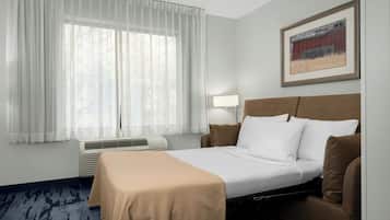 A hotel room with a bed, a bedside table, a lamp, and a window with sheer curtains.