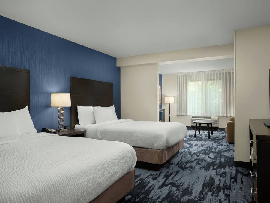 A hotel room with two beds, a desk, a television, and a window with curtains.