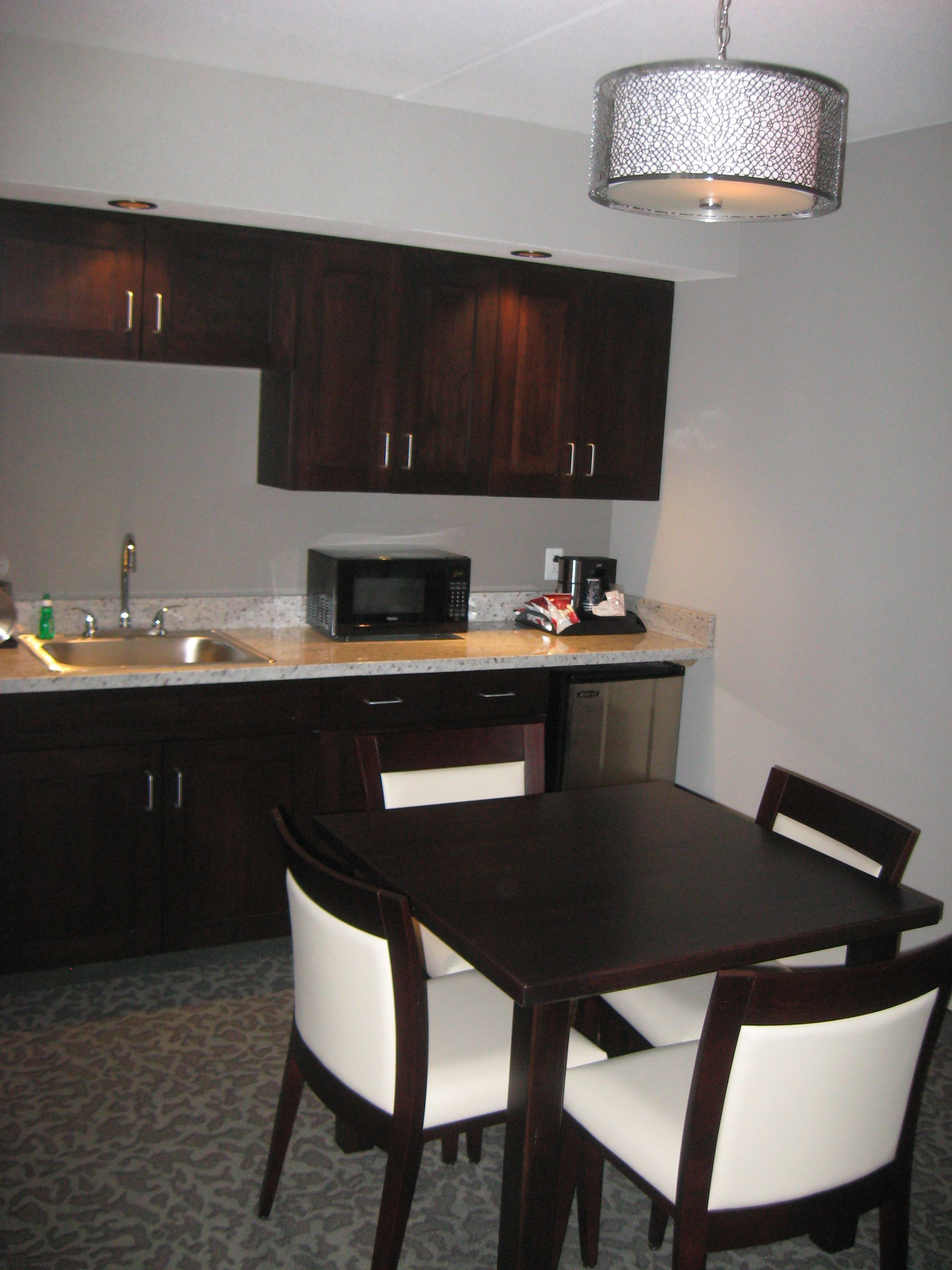 A compact kitchen with dark wooden cabinets, a microwave, a coffee maker, and a dining table with two chairs.