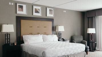 A hotel room with a large bed, two bedside tables with lamps, a chair, and framed artwork on the wall.