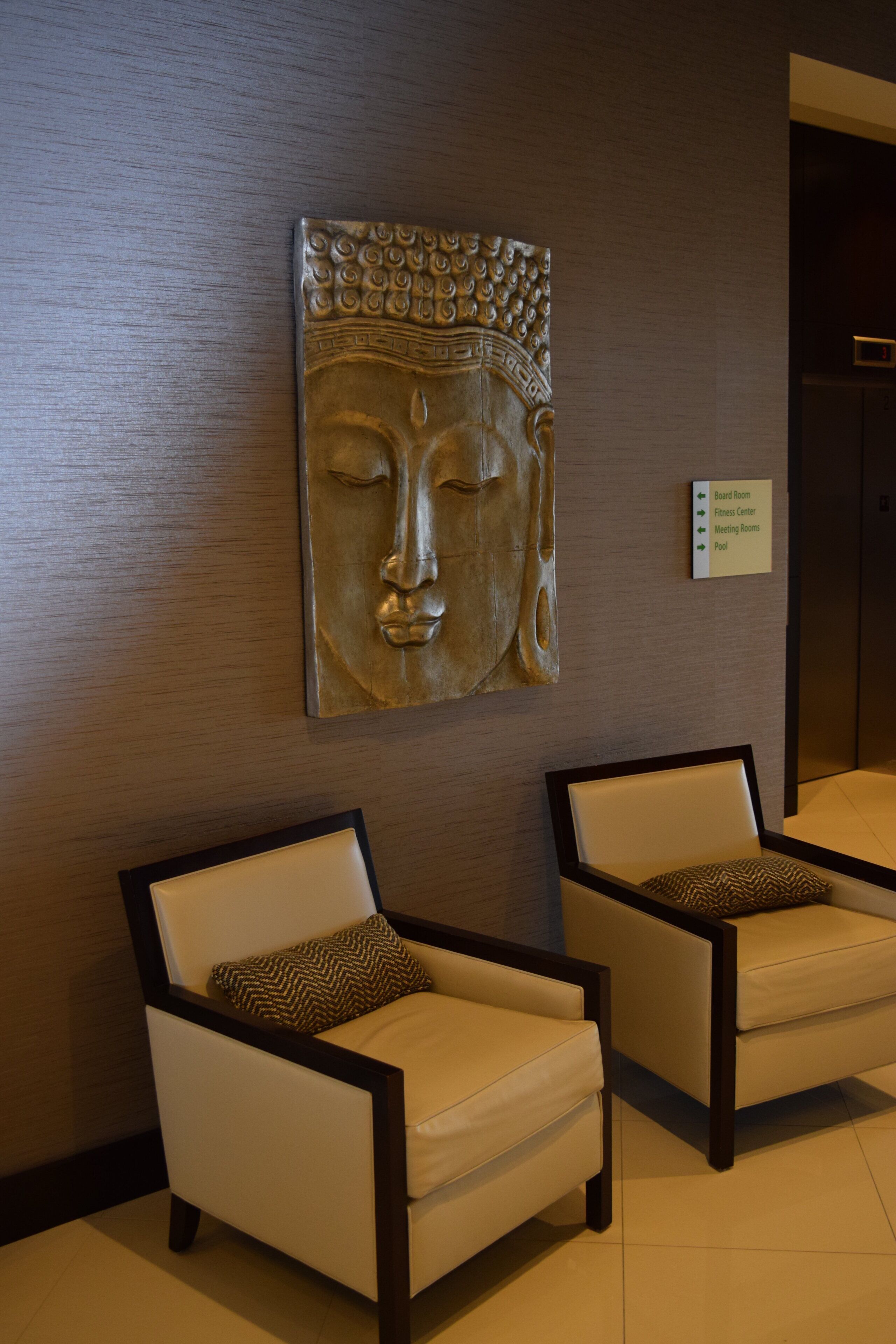 A reception area with two armchairs, a wall-mounted Buddha sculpture, and a directional sign.