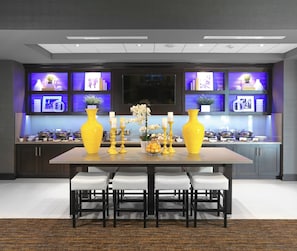 Un espace repas moderne avec une longue table, quatre chaises blanches rembourrées et des vases jaunes.