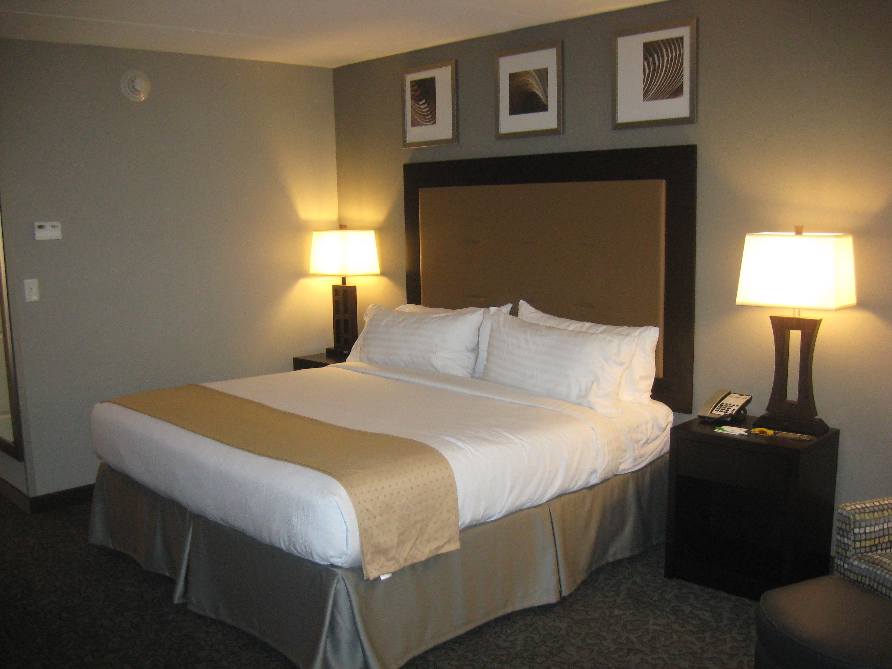 A hotel room with a large bed, two bedside tables with lamps, and three framed pictures on the wall.