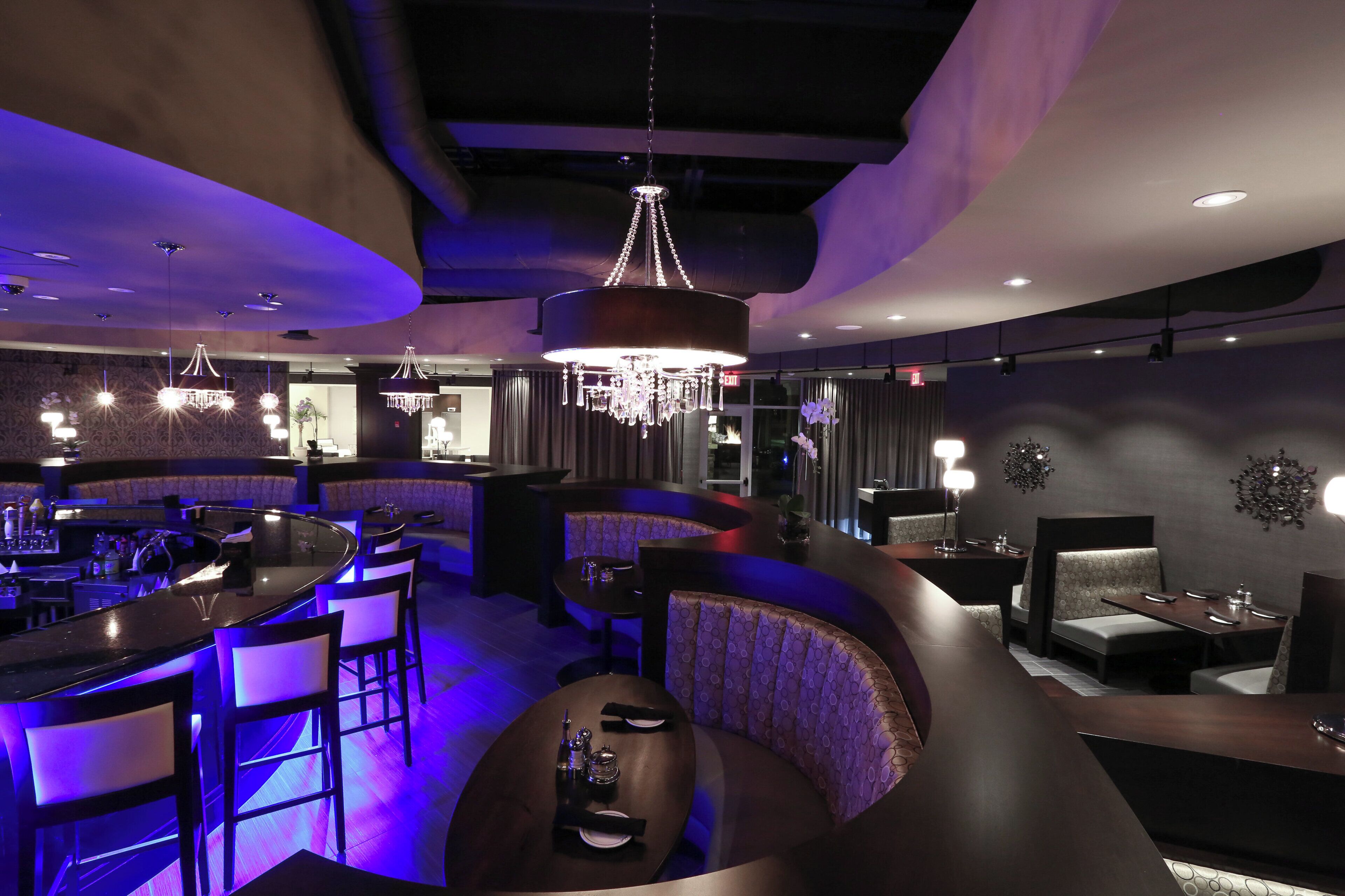 Zona de bar moderna con disposición de asientos curva, iluminación colgante y candelabro.