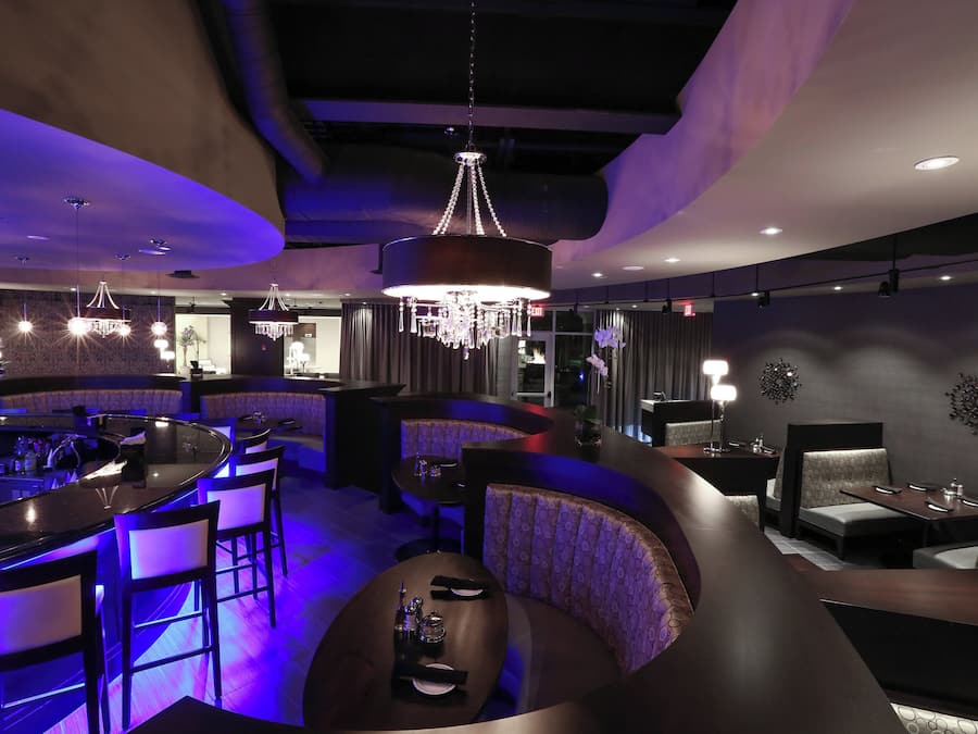 Zona de bar moderna con disposición de asientos curva, iluminación colgante y candelabro.