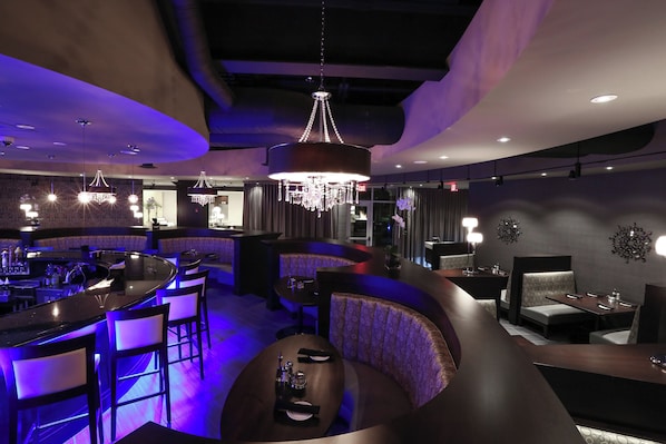 A modern bar area with a curved seating arrangement, pendant lighting, and a chandelier.