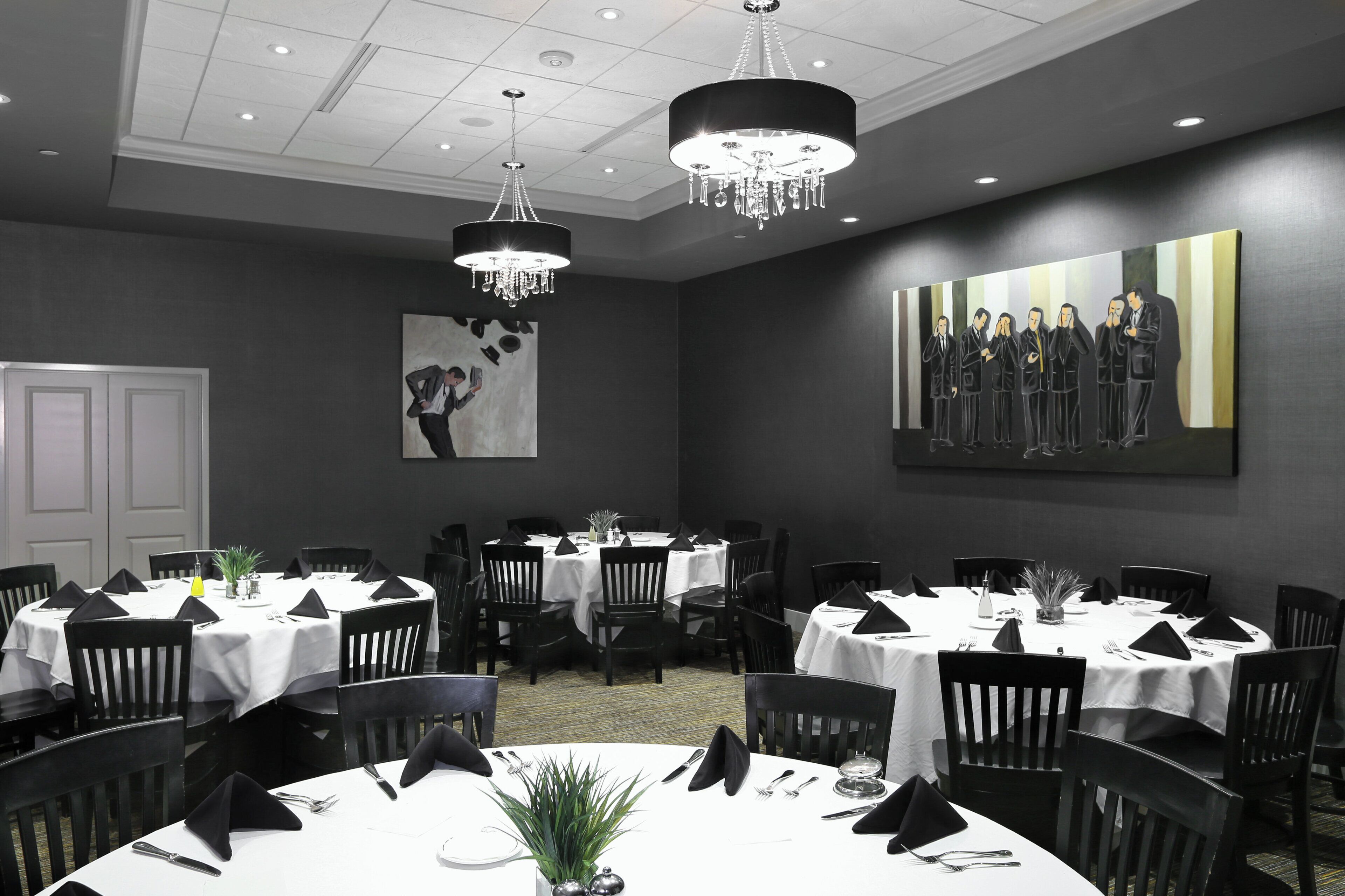 A conference room with multiple tables set for dining, a chandelier, and a large painting on the wall.