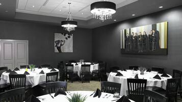 A conference room with multiple tables set for dining, a chandelier, and a large painting on the wall.