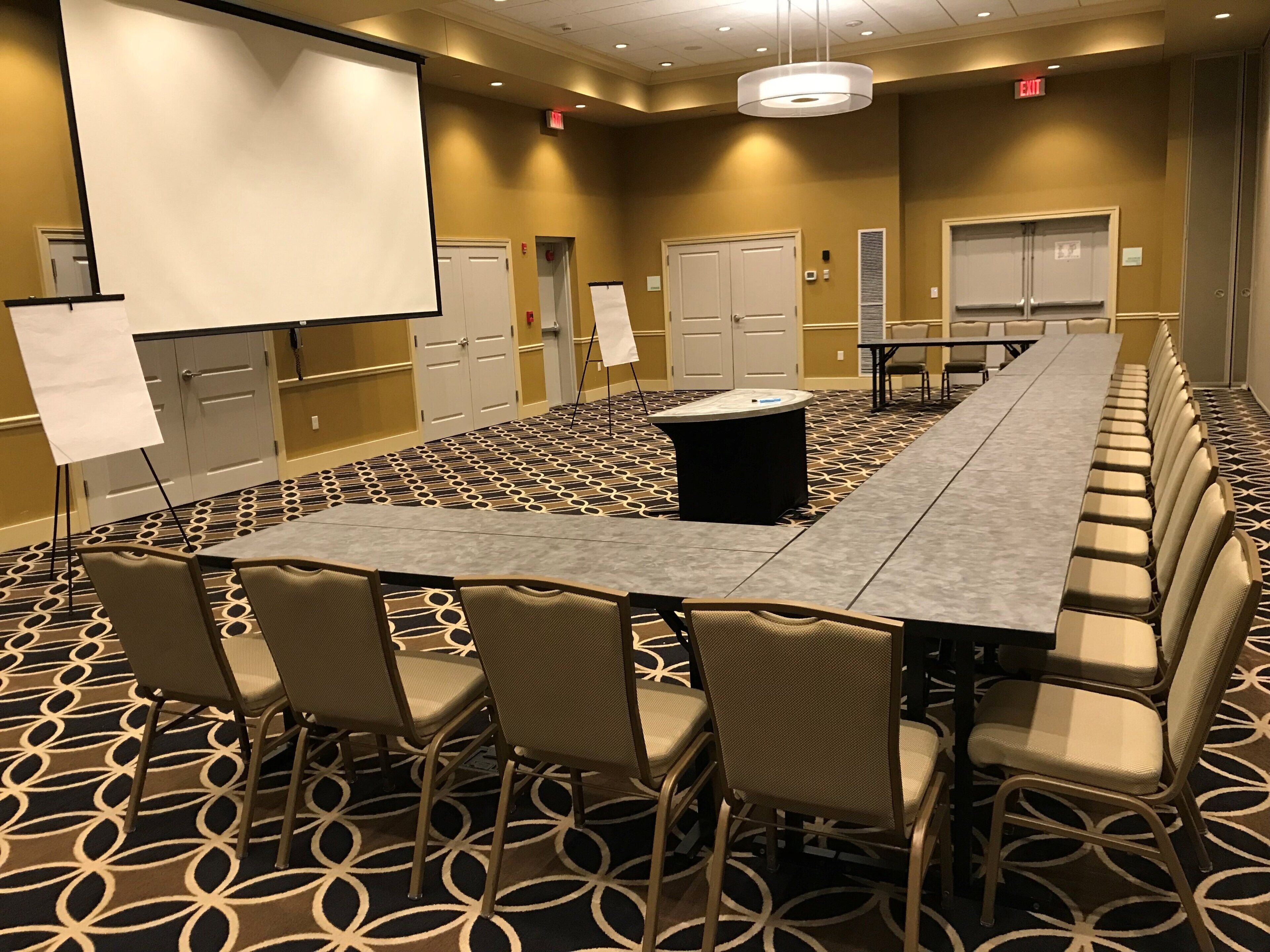 A conference room with a long table, chairs, a projector screen, and a carpeted floor.