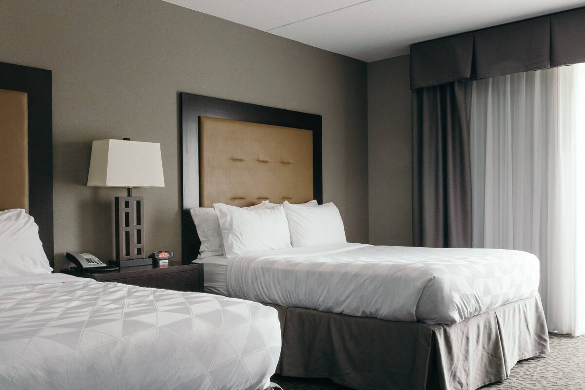 Une chambre d’hôtel avec deux lits, une table de chevet avec une lampe, un téléphone et une tête de lit.