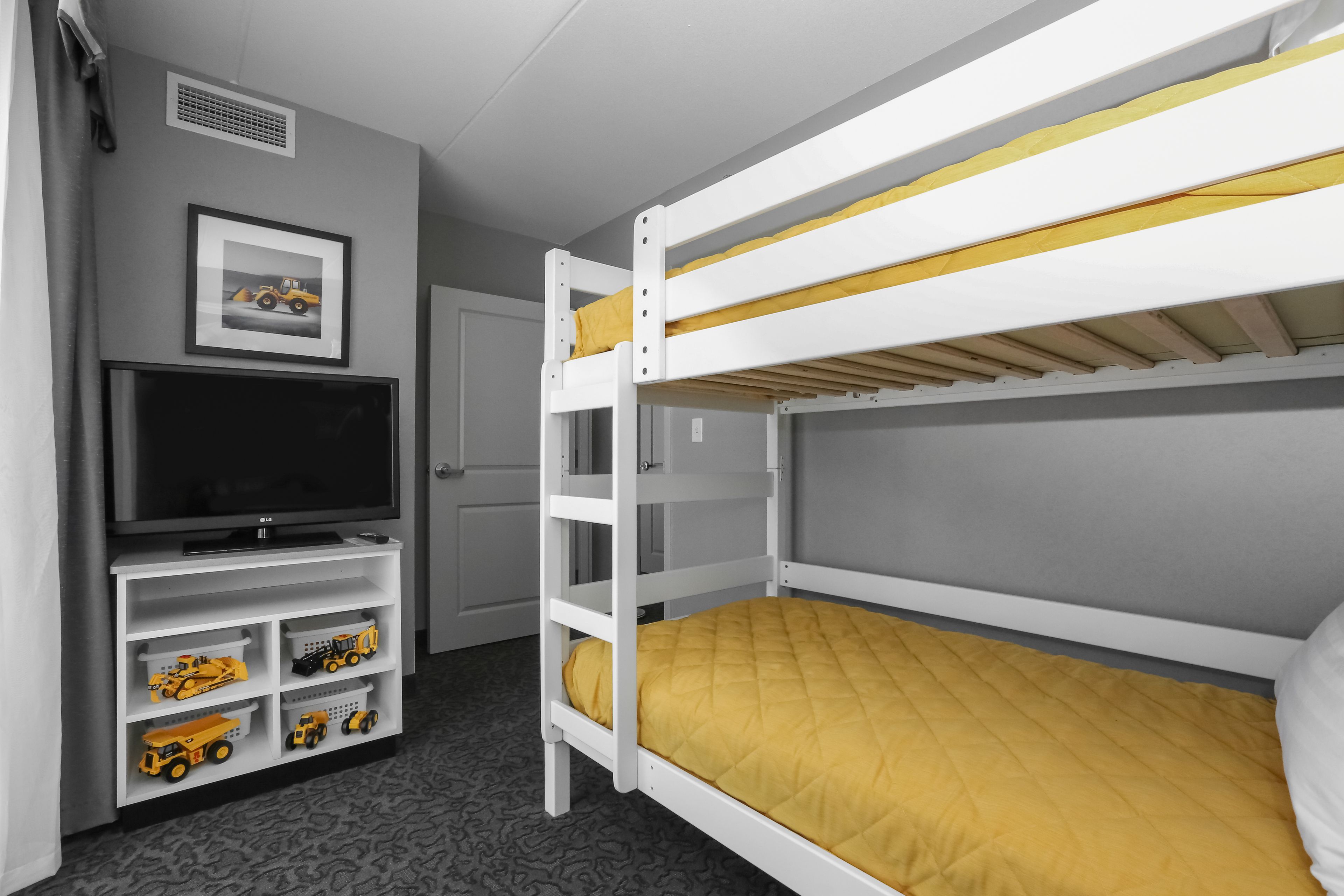 A bunk bed with a yellow mattress, a TV on a stand below, and toy vehicles in storage compartments.