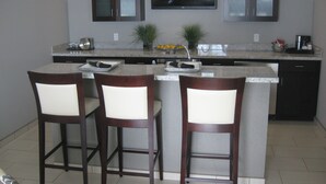 A kitchen with a central island, two bar stools, a flat-screen TV, and pendant lights. - Holiday Inn Hotel & Suites East Peoria by IHG (East Peoria)