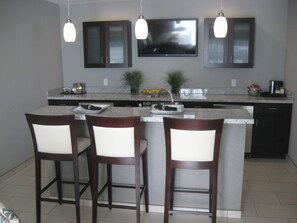 A kitchen with a central island, two bar stools, a flat-screen TV, and pendant lights. - Holiday Inn Hotel & Suites East Peoria by IHG (East Peoria)