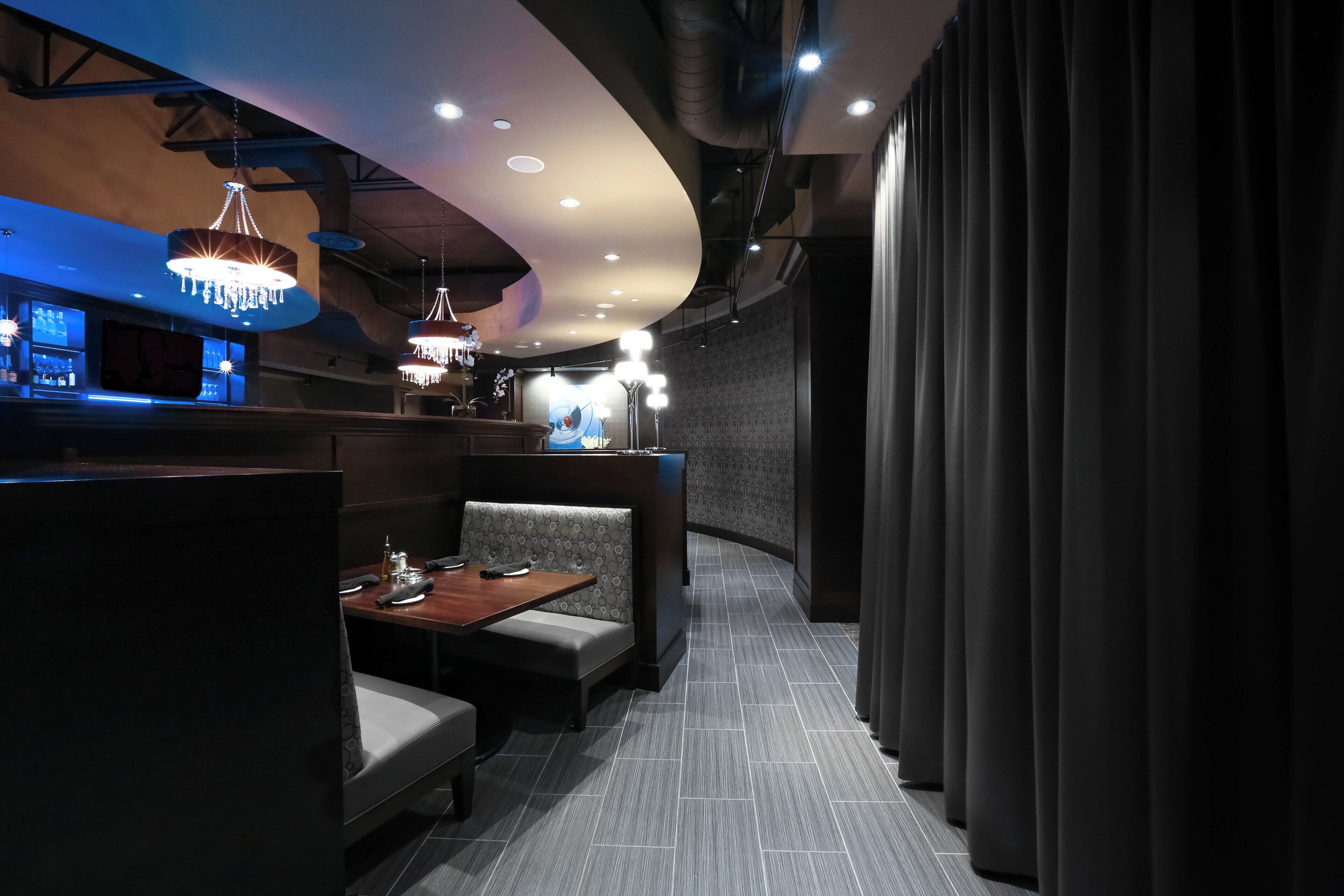 Un interior de restaurante con cabinas, mesas y candelabros colgantes.