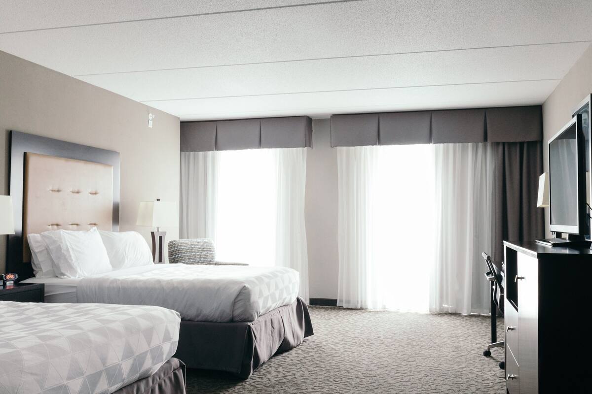 Une chambre d’hôtel avec deux lits, un bureau, une télévision et de grandes fenêtres équipées de rideaux.