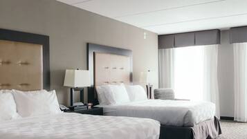 Habitación de hotel con dos camas, una mesita de noche con lámpara, un reloj y una ventana con cortinas.