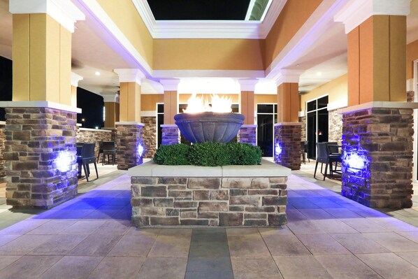 A stone fountain with a fire feature, surrounded by stone pillars and a tiled floor, in a well-lit indoor area. - Holiday Inn Hotel & Suites East Peoria by IHG (East Peoria)