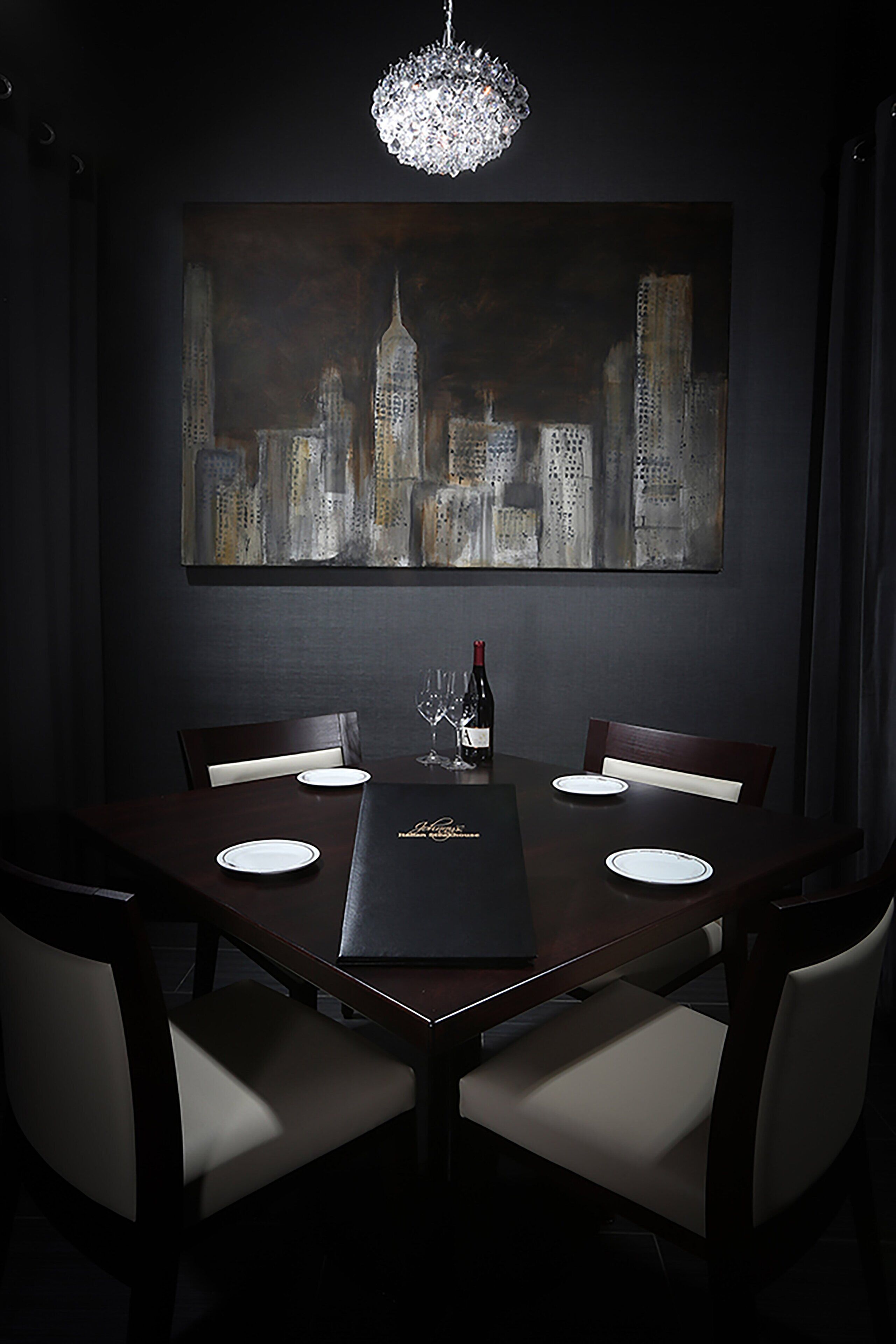 A dining area with a dark wood table, white chairs, a chandelier, and a cityscape painting on the wall.