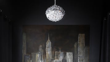 A dining area with a dark wood table, white chairs, a chandelier, and a cityscape painting on the wall.