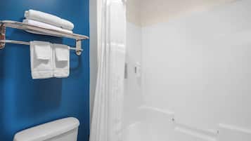 A bathroom with a blue wall, a white toilet, a shower with a white curtain, and a towel rack with folded towels.