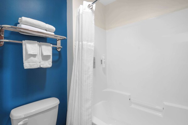 A bathroom with a blue wall, a white toilet, a shower with a white curtain, and a towel rack with folded towels.