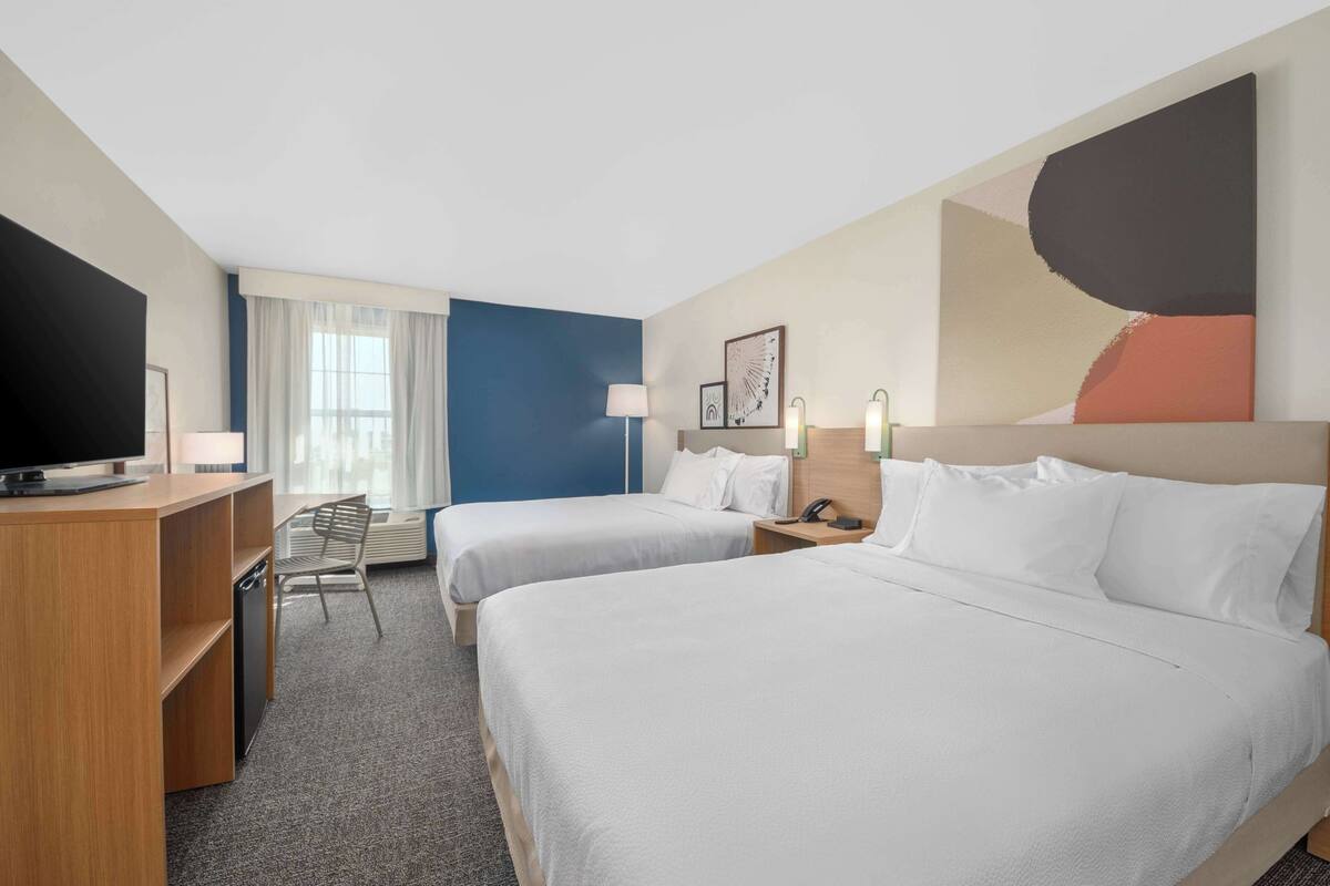 A hotel room with two beds, a desk, a chair, and a television.
