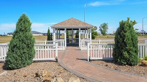 A gazebo with a brick pathway leading to it, surrounded by white railings and two evergreen trees. - Spark by Hilton Minot (Minot)