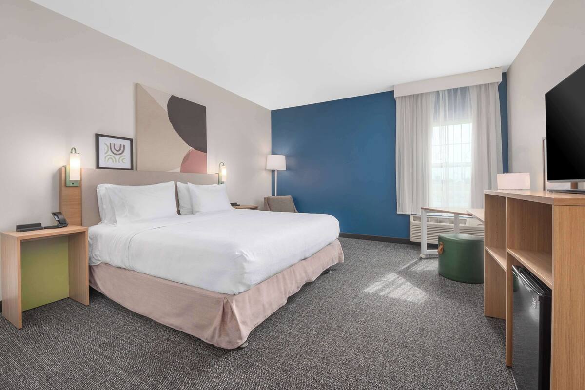 A hotel room with a bed, bedside tables, a desk, a television, and a window with curtains.