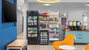 A modern cafe with seating, a refrigerator stocked with snacks, a microwave, and a coffee station. - Spark by Hilton Minot (Minot)
