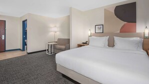 A hotel room with a large bed, a desk, a chair, a lamp, and a painting on the wall. - Spark by Hilton Minot (Minot)
