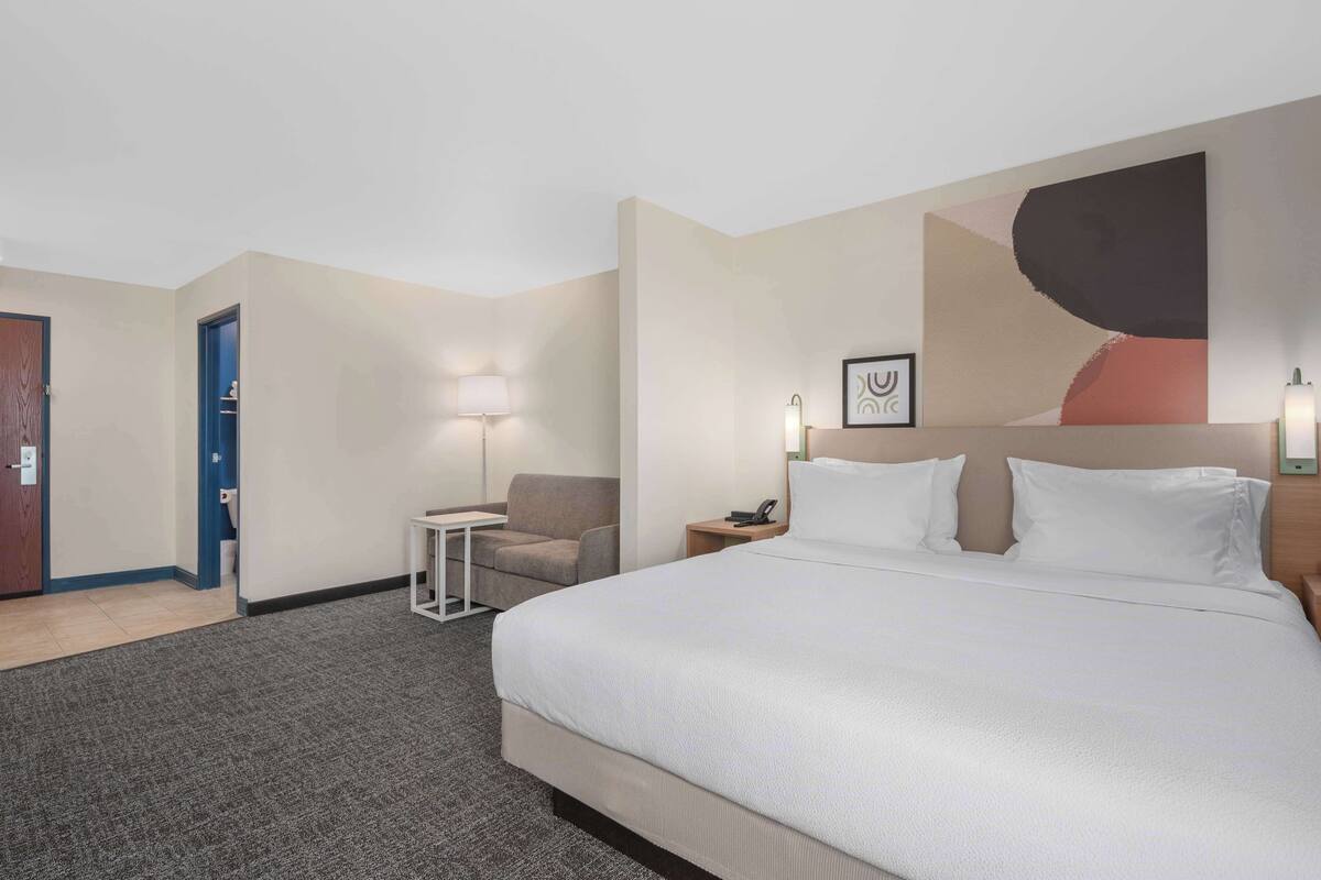 A hotel room with a large bed, a desk, a chair, a lamp, and a painting on the wall.