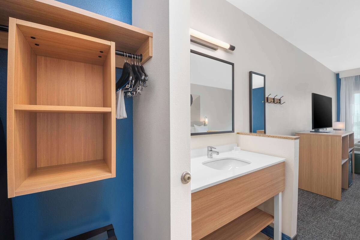 A modern bathroom with a wooden vanity, a large mirror, and a television.