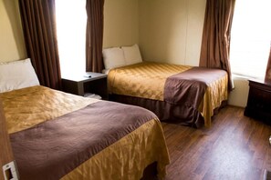 A hotel room with two beds, a nightstand, and a window with curtains. - Cotulla Homes (Cotulla)