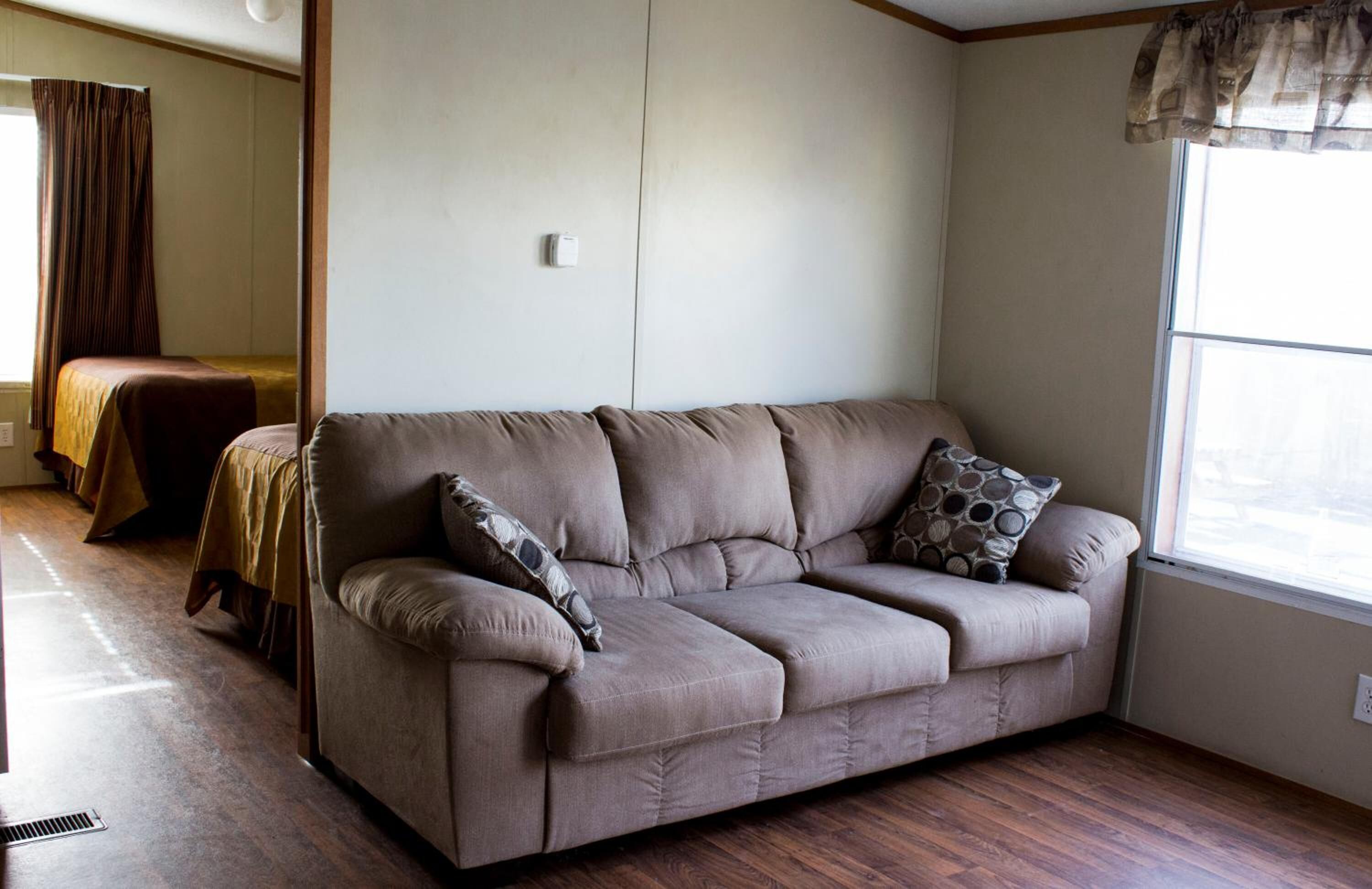 A living room with a sofa, a window, and a bed in the background.