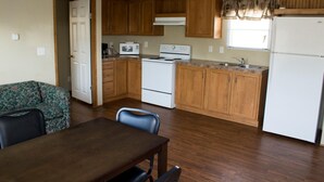 A compact kitchen with wooden cabinets, a stove, a microwave, and a refrigerator. - Cotulla Homes (Cotulla)