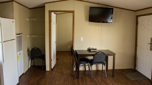 A compact room with a dining table and chairs, a television mounted on the wall, and a refrigerator. - Cotulla Homes (Cotulla)