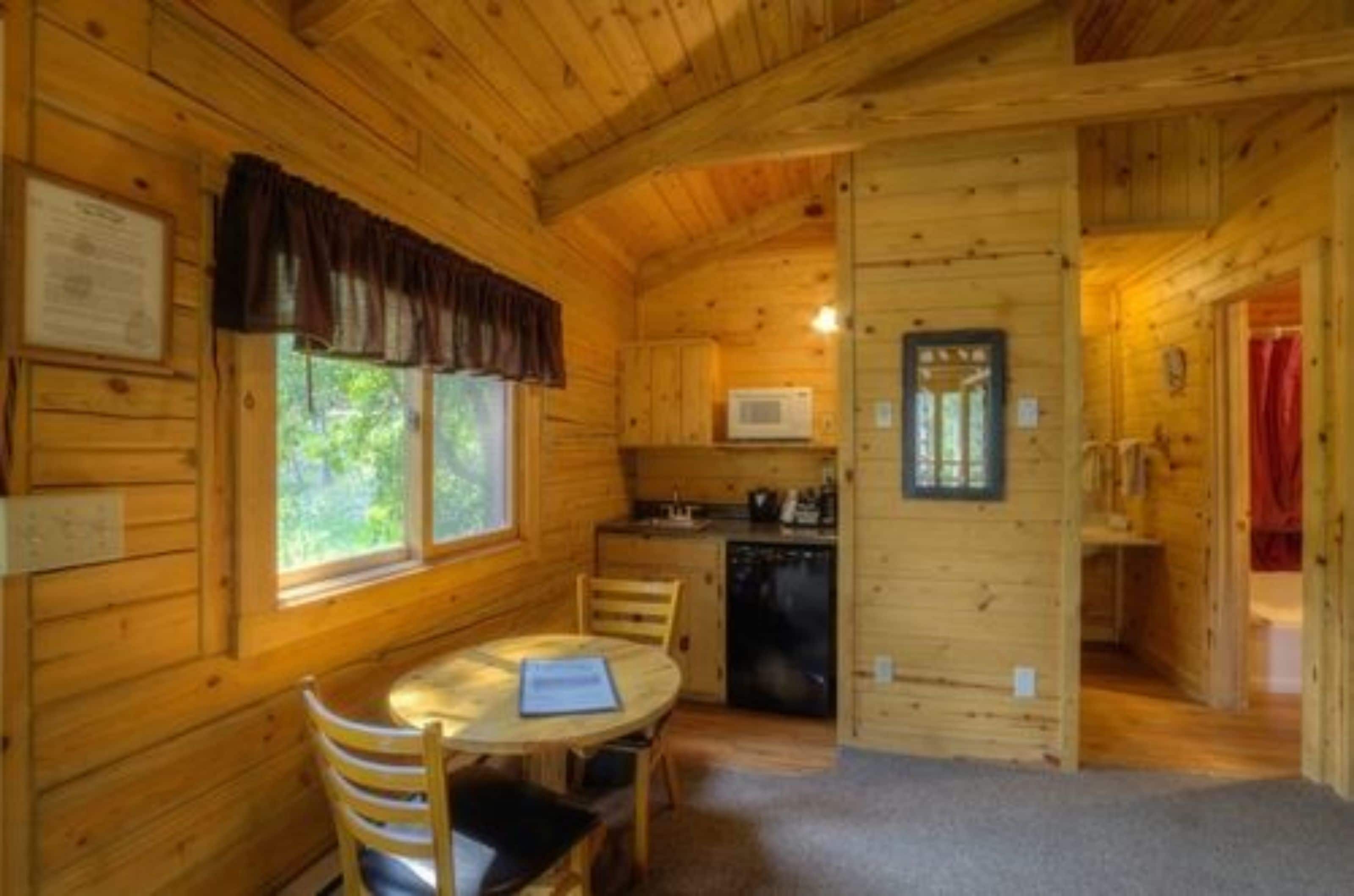 A wooden cabin with a dining area, kitchen, and a small bathroom.