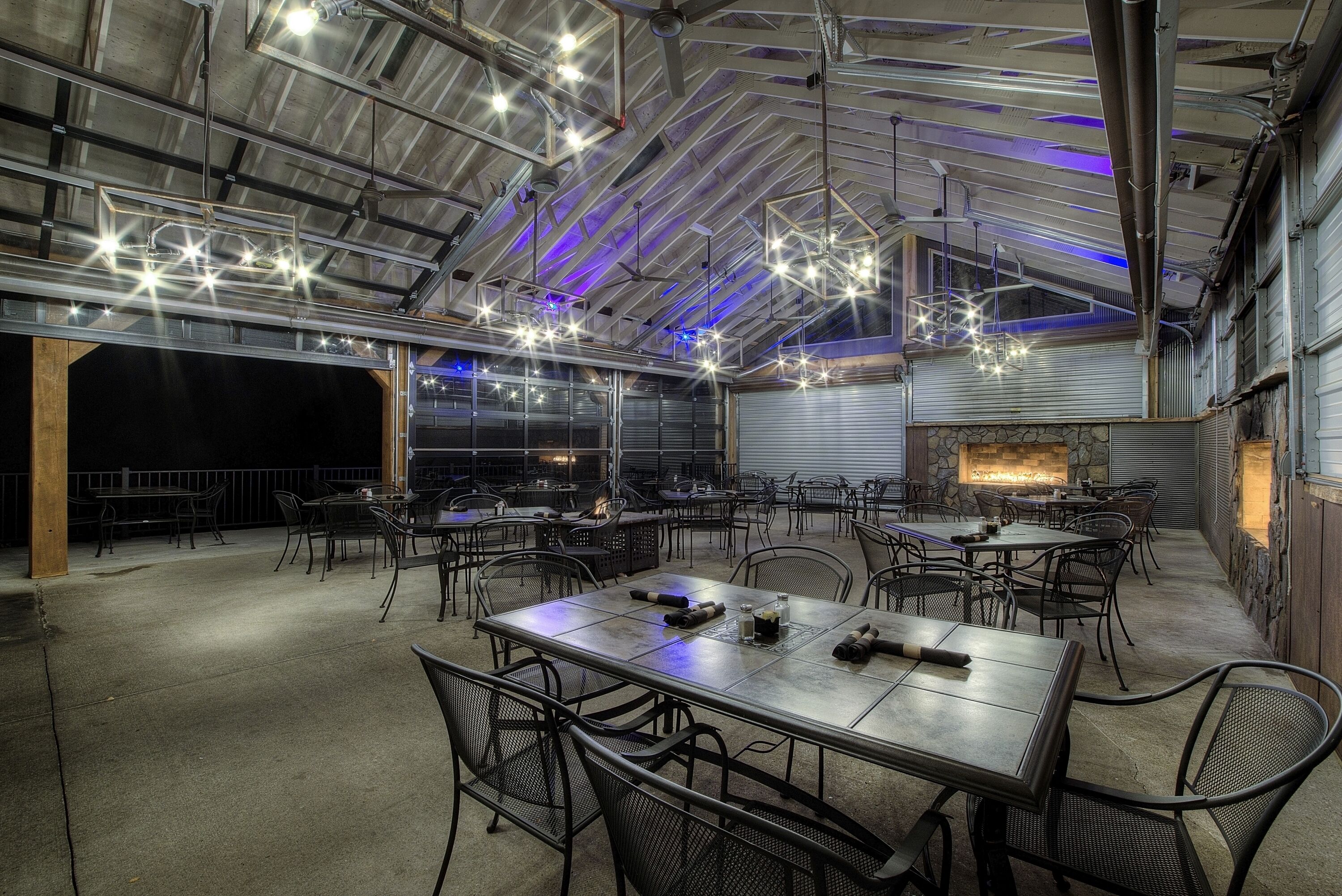 An indoor dining area with tables and chairs, a ceiling with exposed beams, and hanging lights.