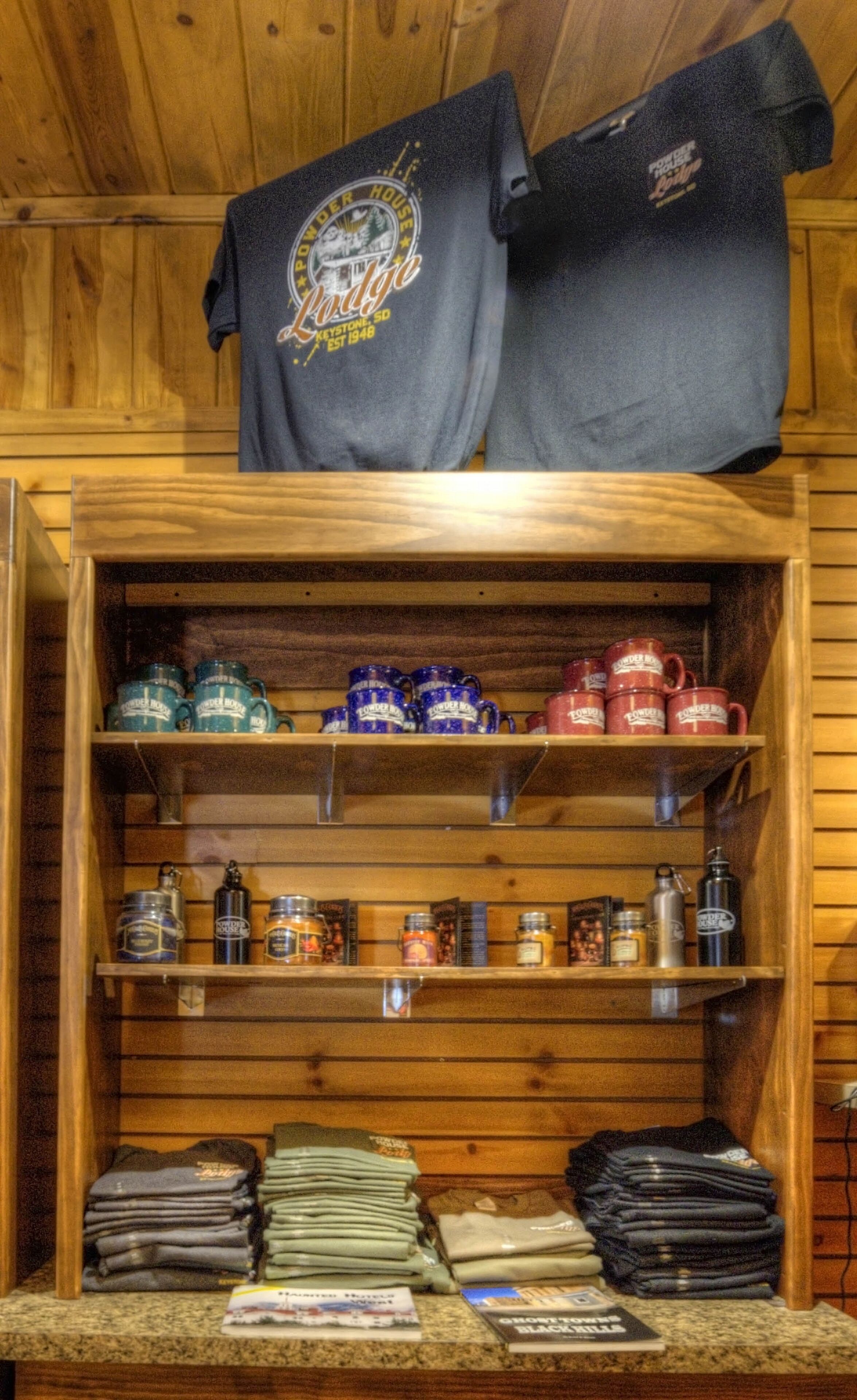A display of merchandise including t-shirts, mugs, and folded items in a wooden cabinet.