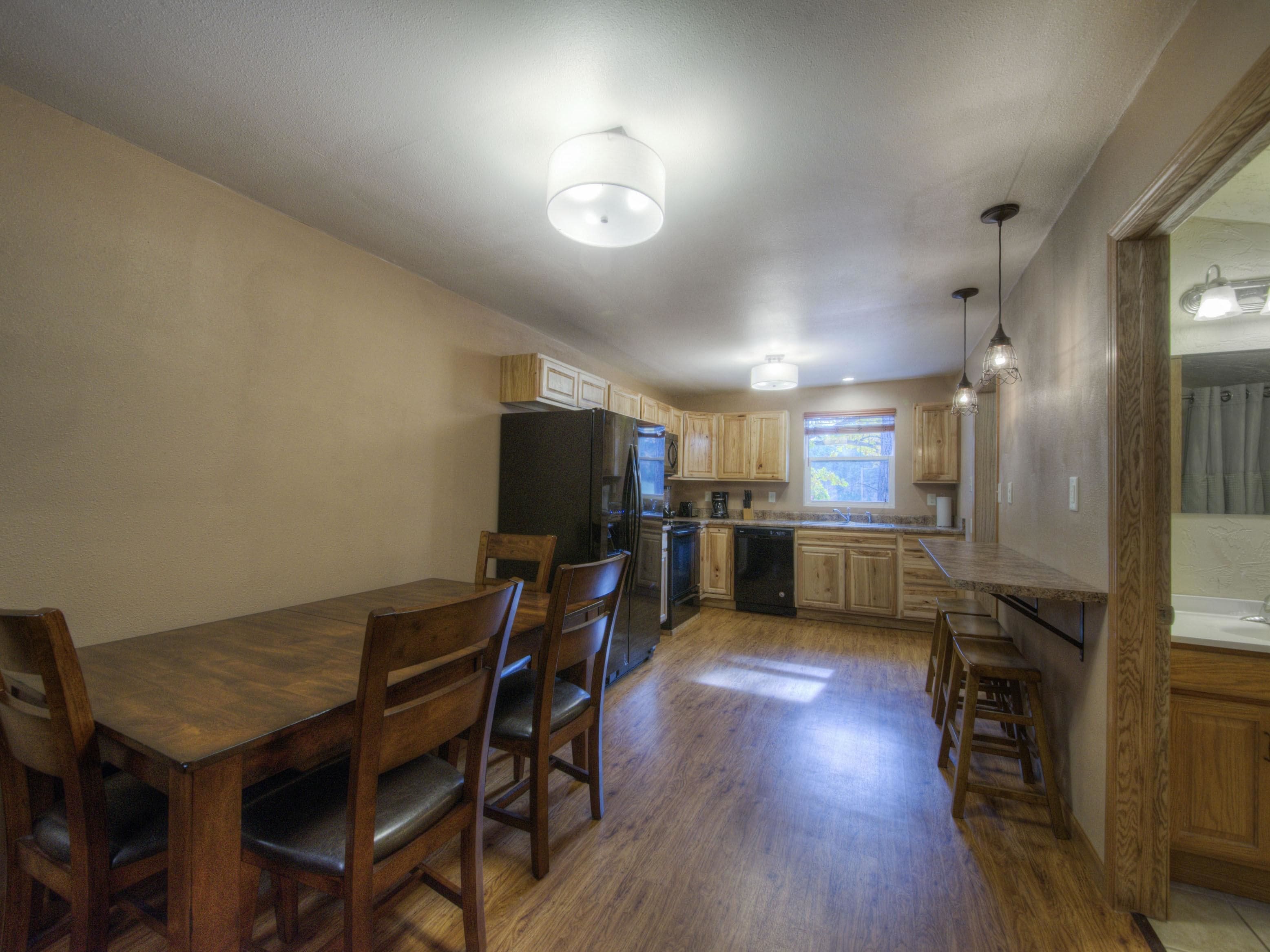 A kitchen with wooden cabinets, a refrigerator, a dishwasher, and a dining area with a table and chairs.