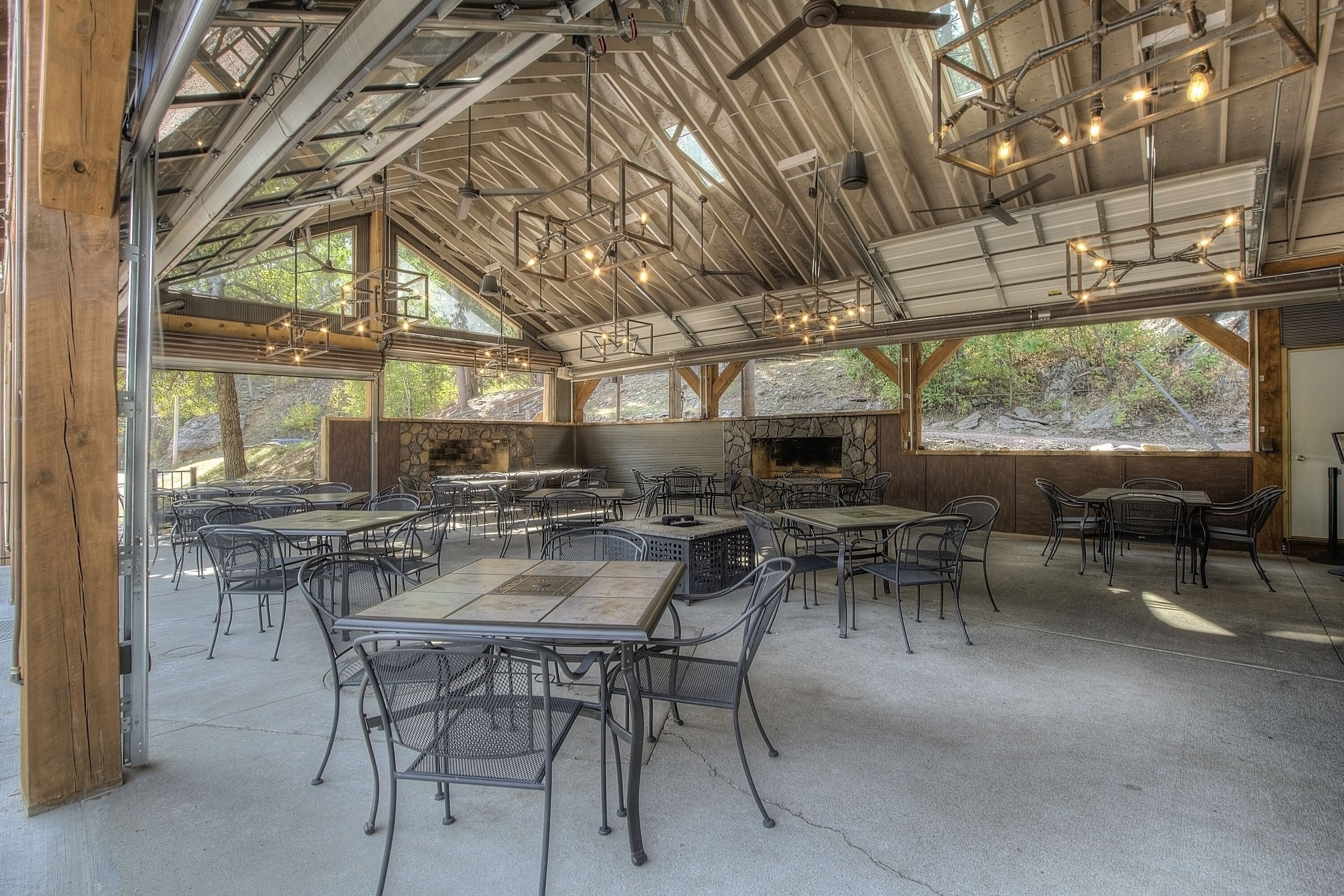 Un espace de restauration en plein air doté de plusieurs tables et chaises, d’une cheminée en pierre et offrant une vue sur le paysage environnant.