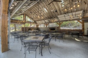 Area pranzo all'aperto con diversi tavoli e sedie, un camino in pietra e vista sul paesaggio circostante.