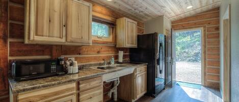Una cocina estilo cabaña de madera con alacenas empotradas, microondas, lavaplatos y refrigerador.