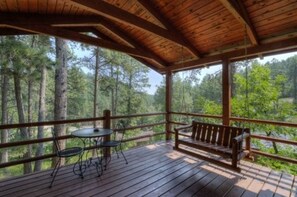A wooden deck with a table and chairs, overlooking a forest.