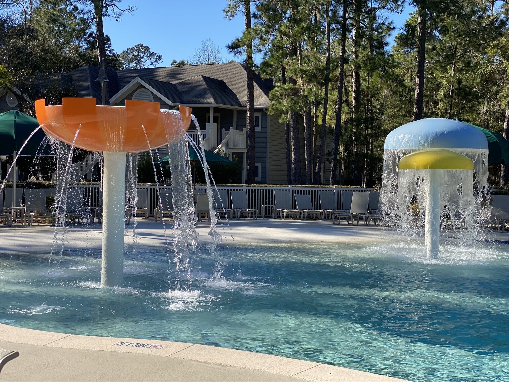 A water feature with two fountains in a pool area, surrounded by lounge chairs and a building in the background.