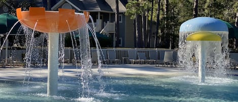 A water feature with two fountains in a pool area, surrounded by lounge chairs and a building in the background.