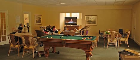 A pool room with a pool table, a foosball table, and a television in the background.