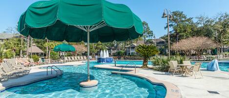 A swimming pool with lounge chairs and umbrellas, surrounded by palm trees and houses.